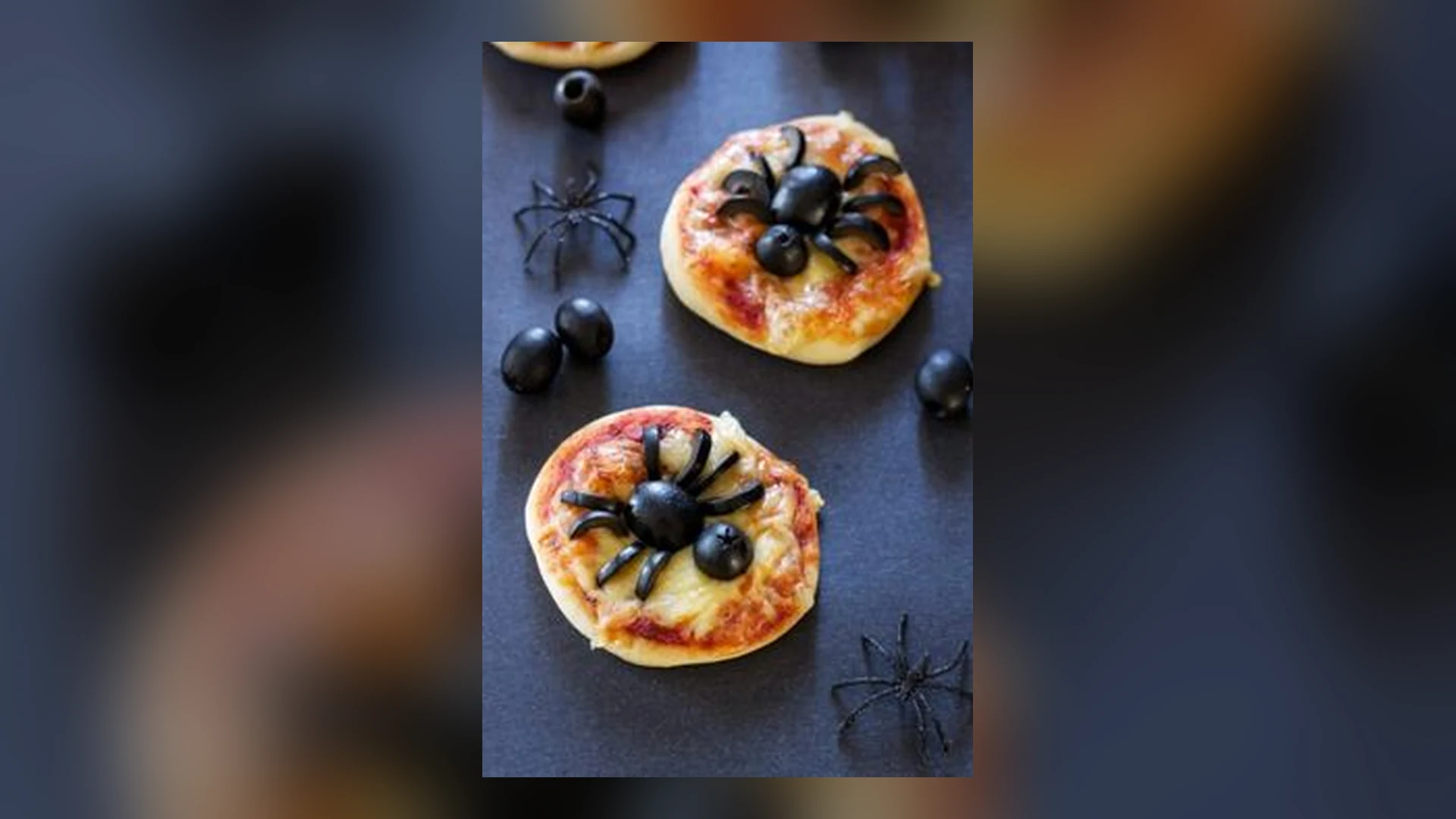 Imagen del taller Cocina Terrorífica Halloween 2026: dos minipizzas con una araña hecha con aceitunas negras sobre una mesa oscura, rodeadas de aceitunas y arañas de juguete